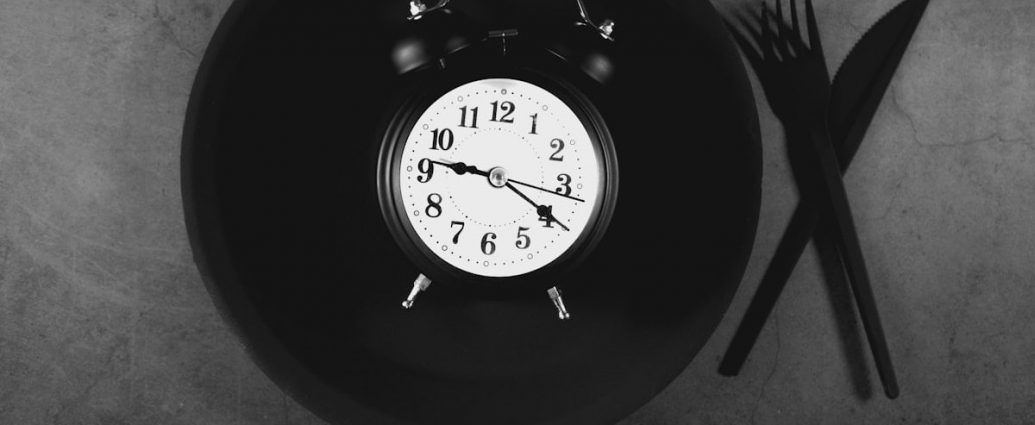 Alarm clock on black plate with cutlery on grey background
