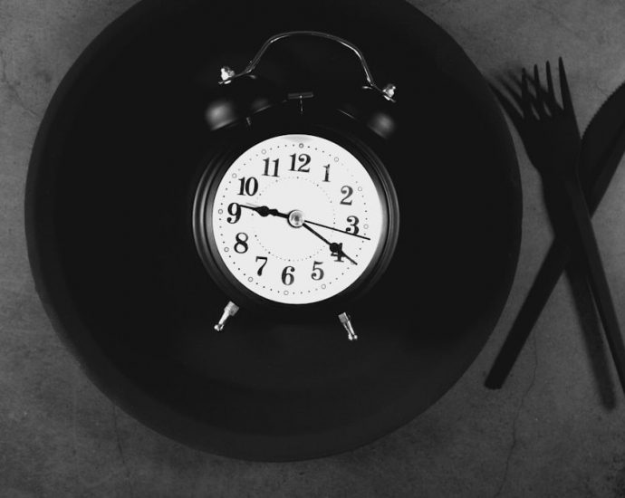 Alarm clock on black plate with cutlery on grey background