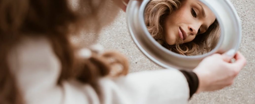 A woman's reflection in a mirror on a city pavement, showing beauty and introspection.