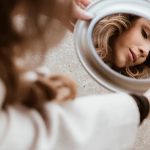 A woman's reflection in a mirror on a city pavement, showing beauty and introspection.
